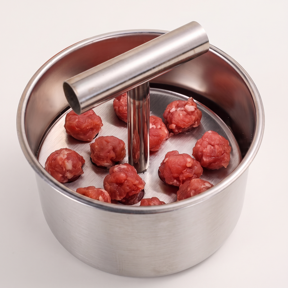 Piston Meatball Press loaded with mince, on a light ground